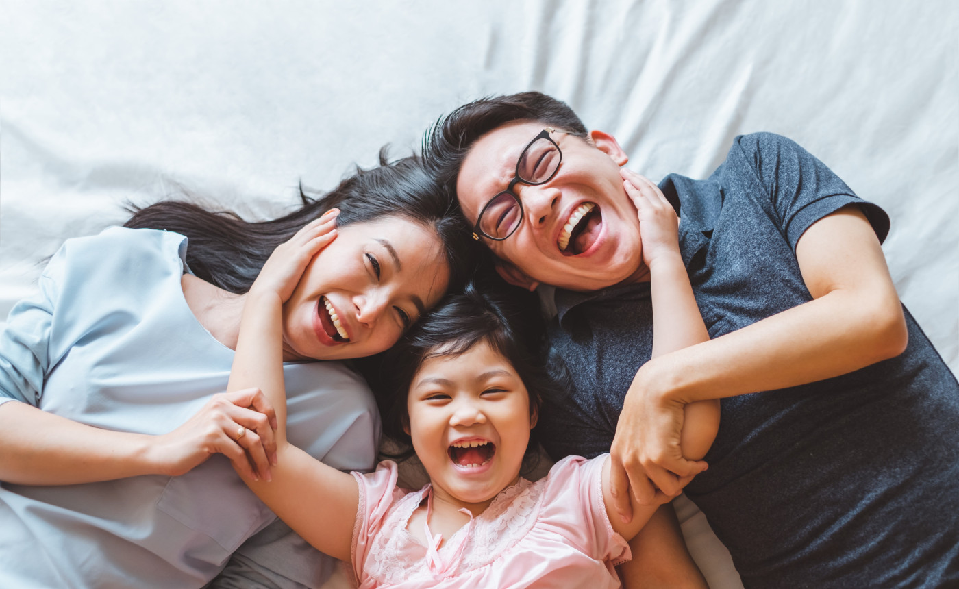 young asian parents with young daughter laughing on the bed